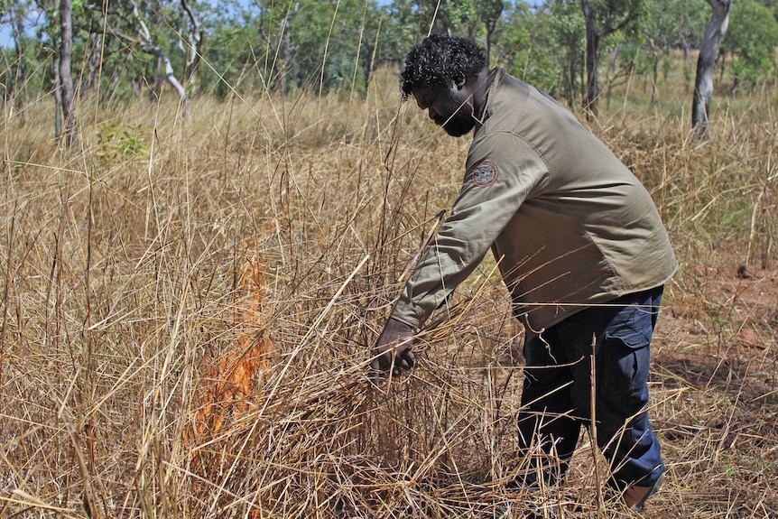 a man lighting a fire in dry grass