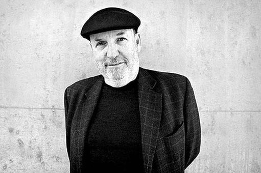 artistic monochrome of man wearing black suit jacket and black beret standing against wall.