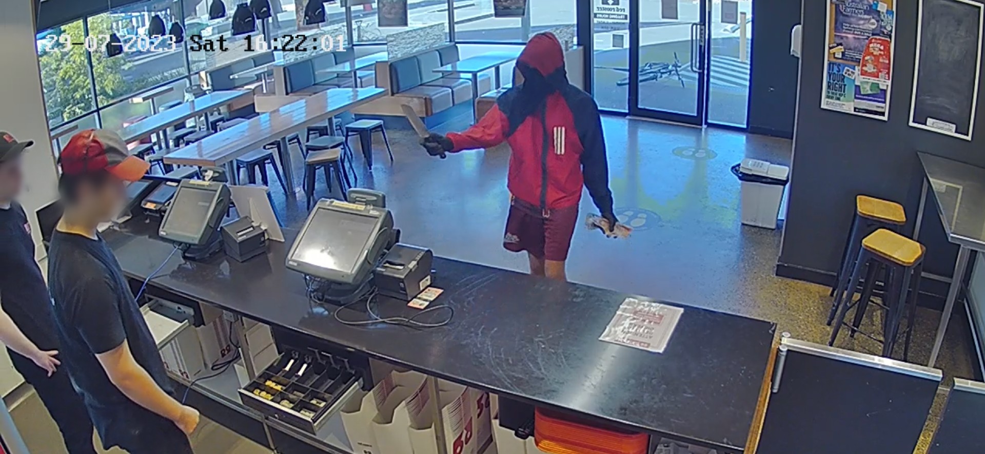 Man holds knife to staff behind counter of fast food restaurant.