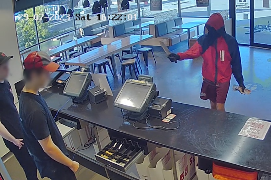 Man holds knife to staff behind counter of fast food restaurant.