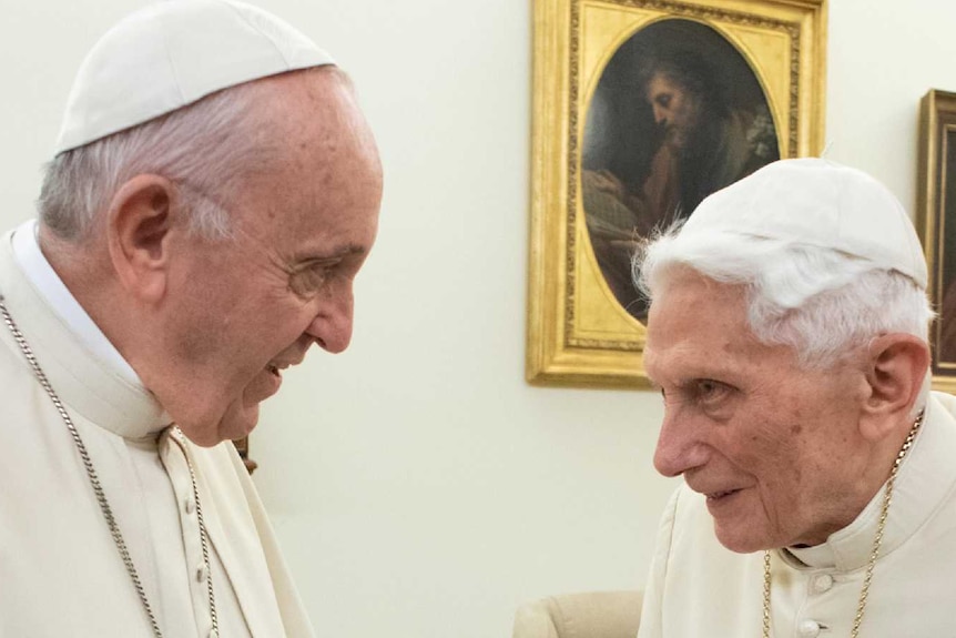Wearing white robes, Pope Frances shakes hands with Pope Emeritus Benedict XVI.