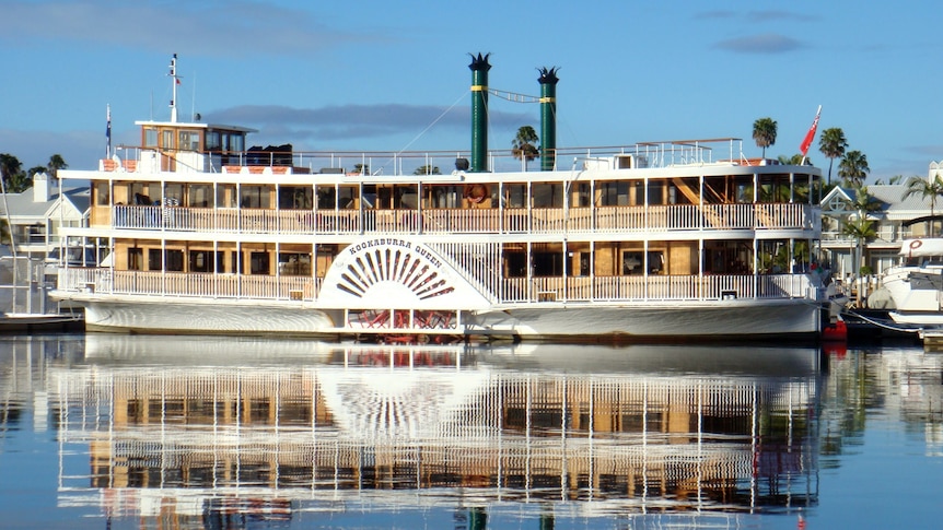 An 80s-era wooden paddlewheeler boat paddles down the murky Brisbane River.