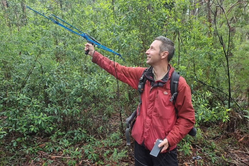 A man in a red rainjacket holding a tracking device 