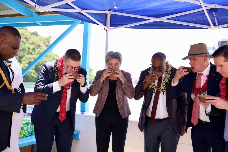 Australian and Vanuatu officials drink from small bowls under a blue tent.