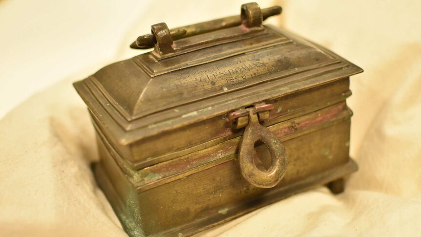 A close-up shot of a rectangular, brass cashbox with words inscribed on the top: 'Glenrowan 1876'.