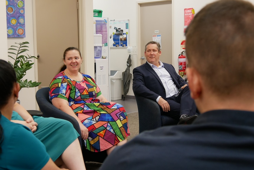A team of lawyers sitting in armchairs in the office. One woman wears a multi coloured dress. On the right is a man in a suit. 