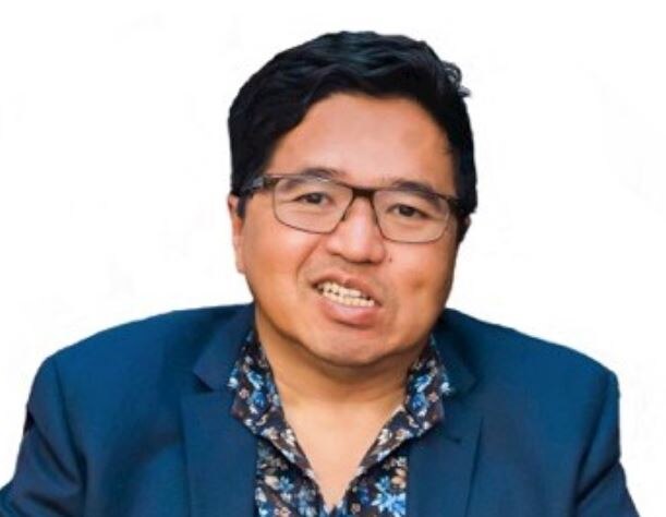 A head shot of Ade who wears a blue suit and glasses