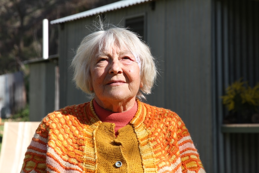 A close-up photo of an elderly woman with white hair in an orange sweater.