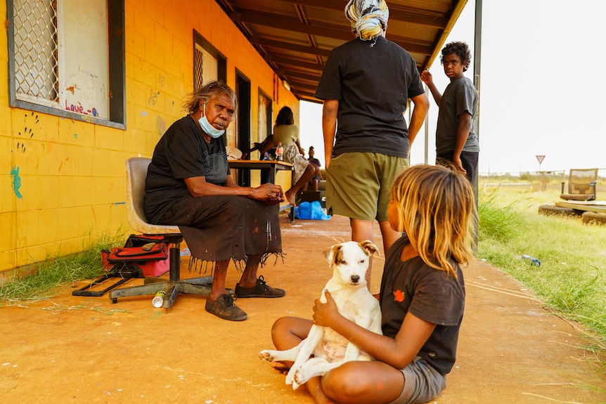 Valerie Martin sits in the Yuendumu community near a child holding a dog.