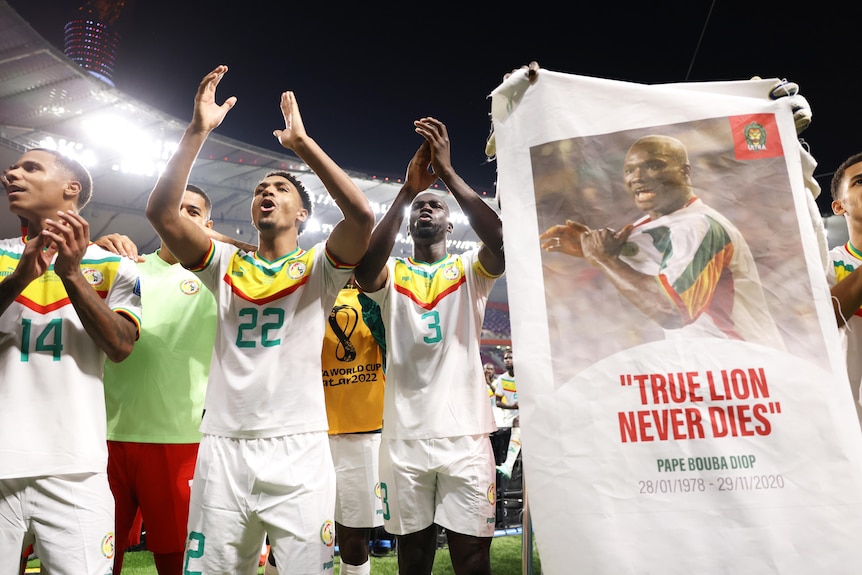 Играчите на Сенегал празнуват близо до публиката с банер, показващ лицето на Papa Bouba Diop и фраза 