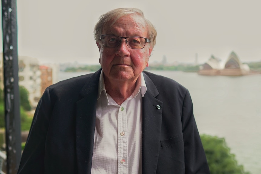 Man wearing a suit and glasses, with the Sydney Opera House in the background. 