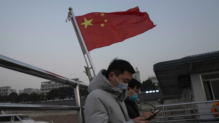 Residents taking the ferry stands near a Chinese national flag in Wuhan