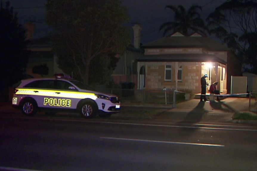 A police SUV outside a cottage with people on the veranda at night