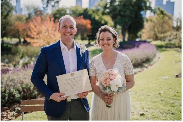 A smiling male and female couple on their wedding day holding their marriage certificate