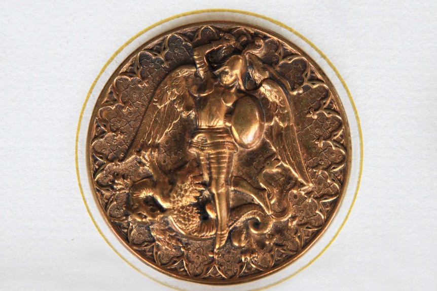 A close-up of a brass button showing Archangel Michael slaying Satan.