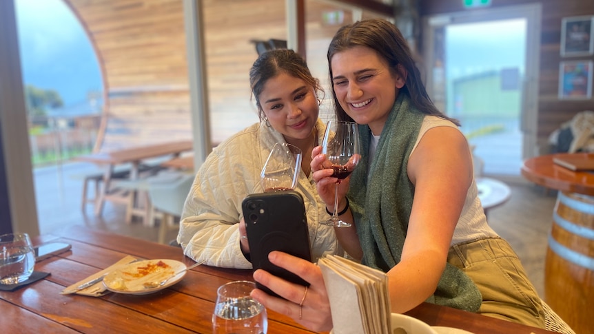 two happy young girls take a selfie and smile into a phone sipping red wine.