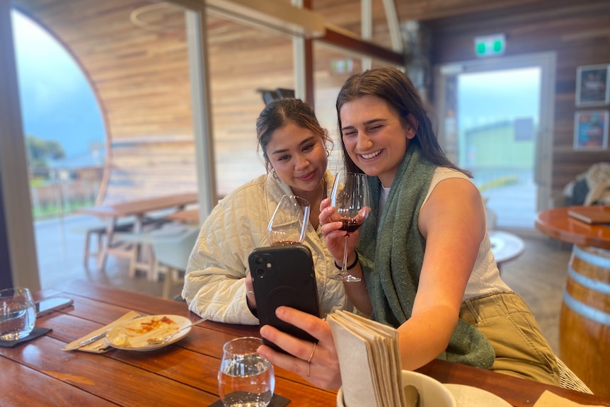 two happy young girls take a selfie and smile into a phone sipping red wine.