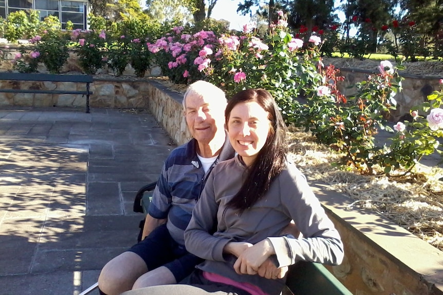 A man and woman smile while sitting outside on a bench.