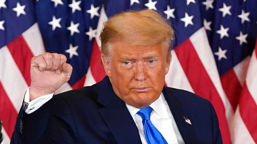 President Donald Trump pumps his fist after speaking in front of the US flag.