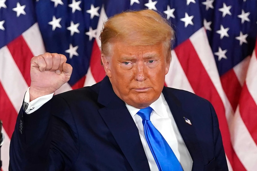 President Donald Trump pumps his fist after speaking in front of the US flag.