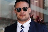A young man with short hair wearing a dark suit, striped tie and sunglasses.