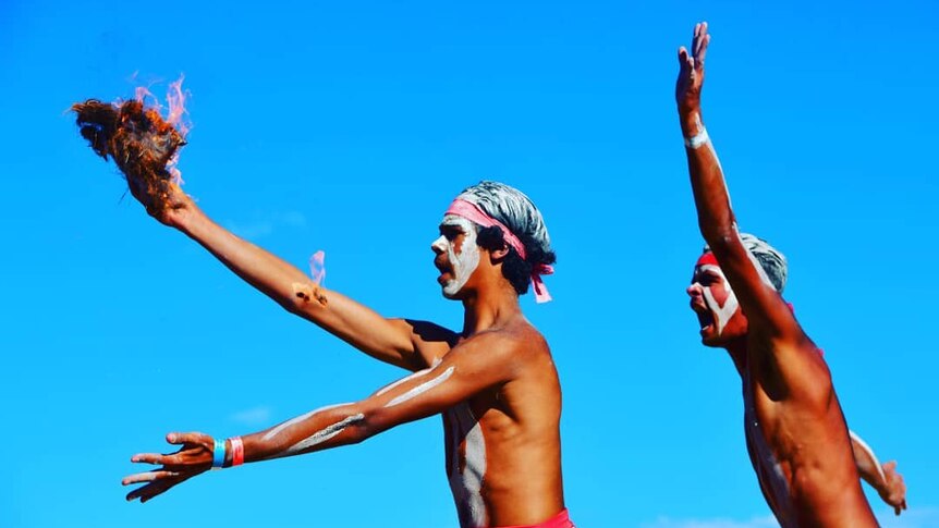 Young indigenous men dance while holding a flame.