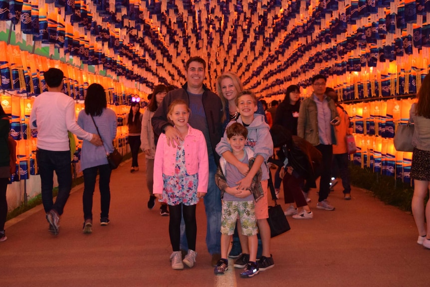Aleathia Holland stands next to her husband and three children in a tunnel filled with glowing lanterns