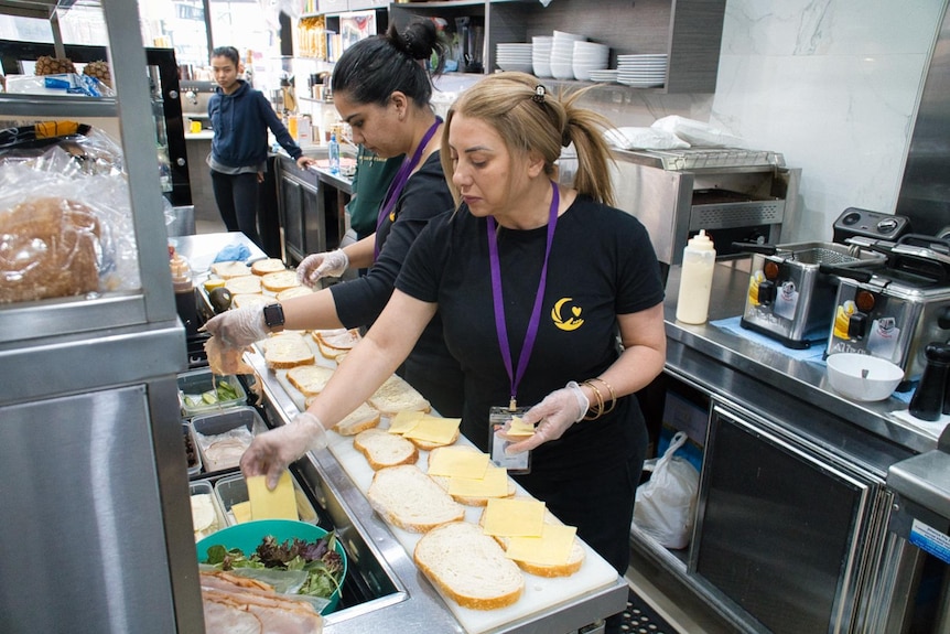 Three volunteers, two of them making bulk sandwiches, the other watching on