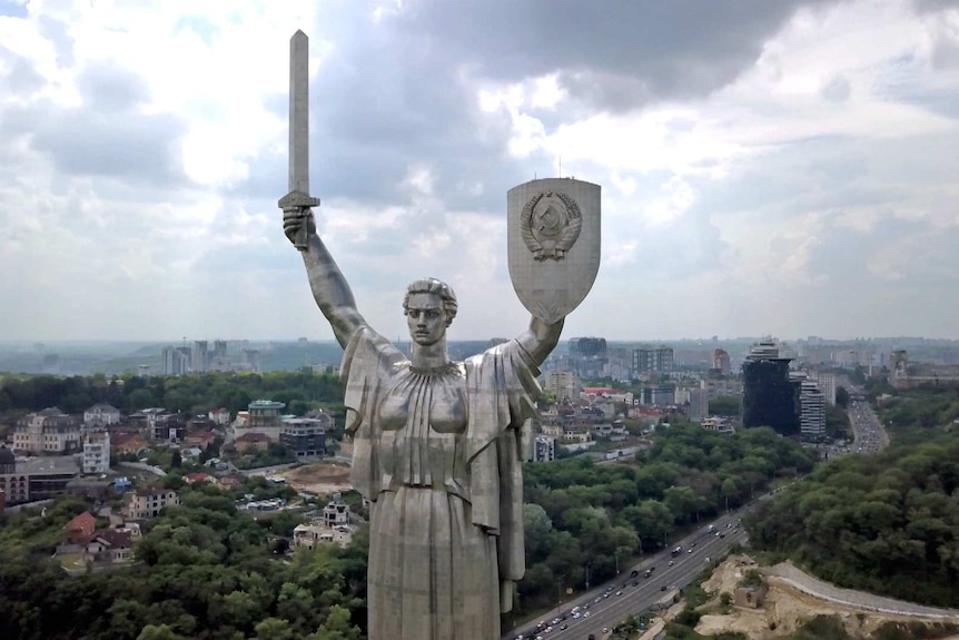 A close up of a stainless steel statue in Keiv, Ukraine depicting a woman holding a sword and a shield.