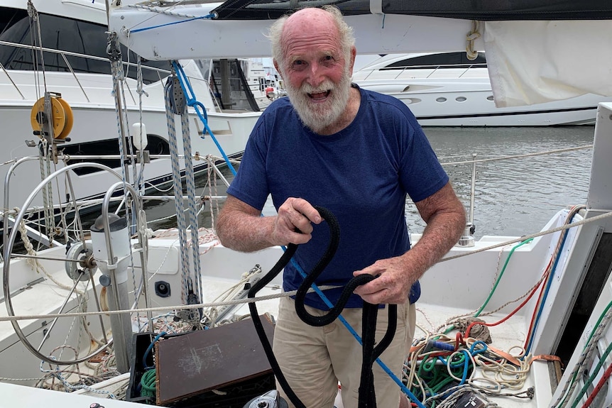 Bald and grey-beared man grins aboard his sailboat while mooring it