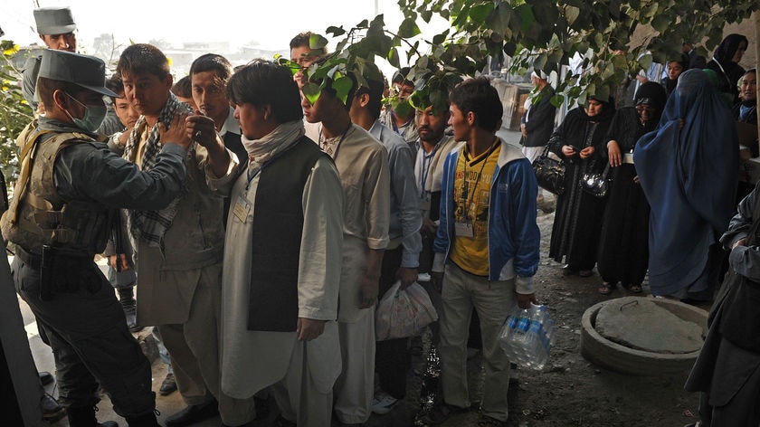 An Afghan policeman searches a young man in queue at a polling station