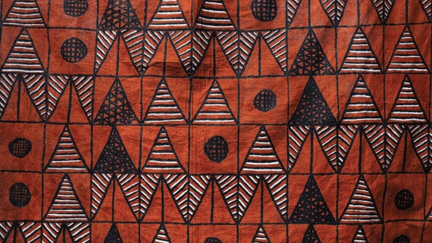 A red tapa cloth design with triangle and circle graphics on it in black and white ink.
