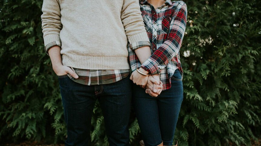 A man and a woman both wearing plaid shirts hold hands.