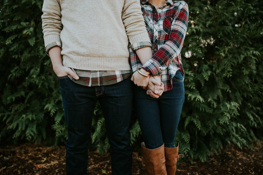A man and a woman both wearing plaid shirts hold hands.
