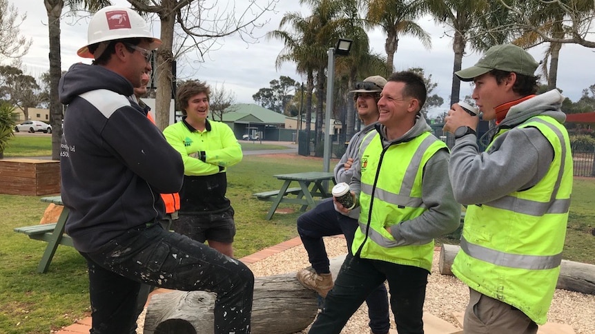 A group of men wearing high vis drink coffee and laugh and talk