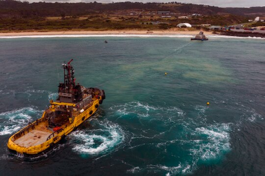Aerial view of yellow tug boat, large concrete structure near shore of King Island