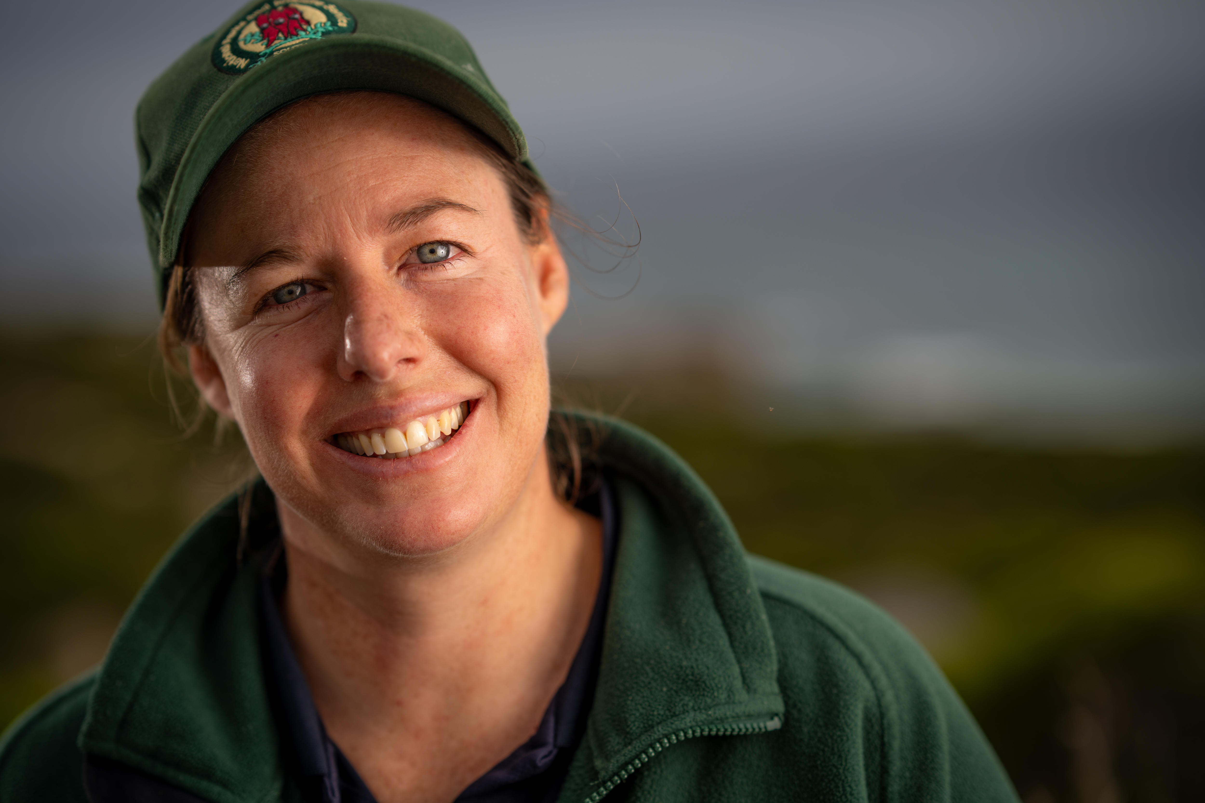 Uma mulher de uniforme verde sorri para a câmera.