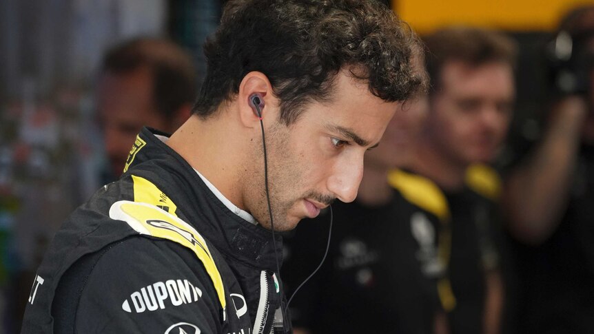 Daniel Ricciardo looks down with a neutral expression on his face with earphones in