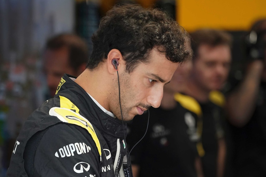 Daniel Ricciardo looks down with a neutral expression on his face with earphones in