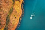 An aerial view of a boat whizzing across a lake.