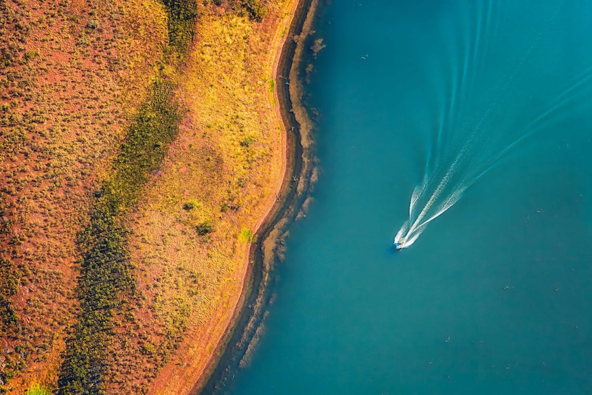 An aerial view of a boat whizzing across a lake.