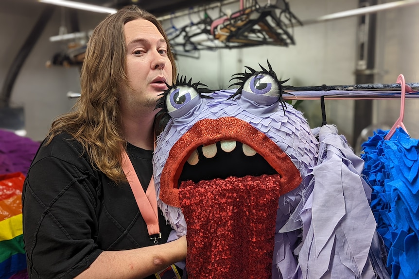 Blake Anderson poses next the head of a purple monster costume with red lips