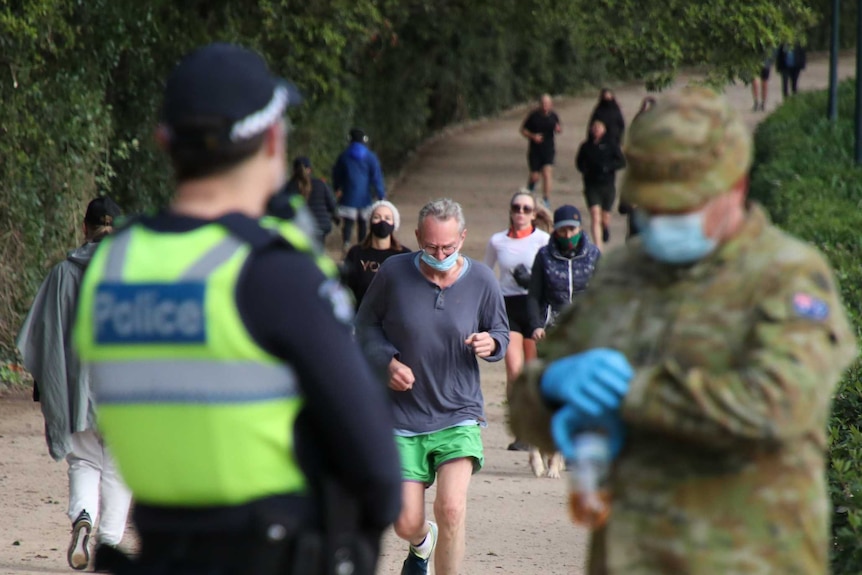 A police officer and an ADF member in the foreground with people running and walking in front of them.
