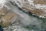 A satellite image shows a dense layer of grey smog over Northern India looming larger than white clouds.