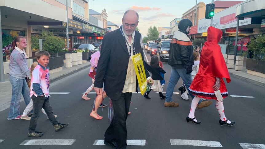 A group of people dressed up as zombies stop traffic and cross over a street in Mount Gambier