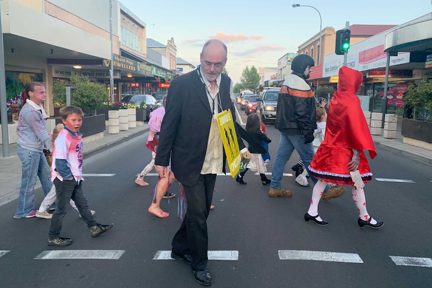 A group of people dressed up as zombies stop traffic and cross over a street in Mount Gambier