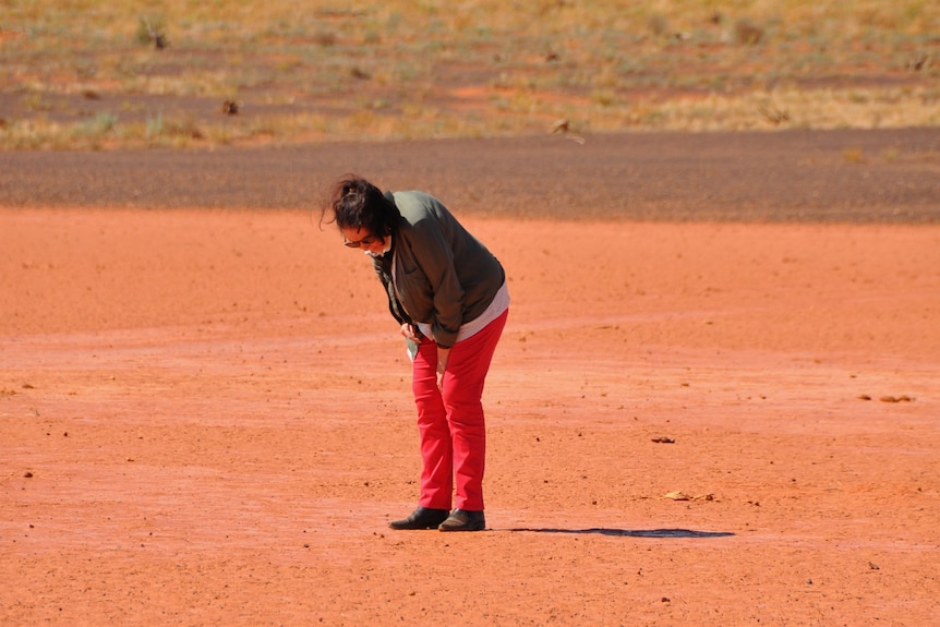 A woman stands in the middle of a flat area surrounded by red soil