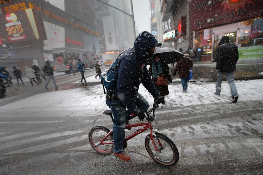 Man rides bicycle through Times Square during New York storm