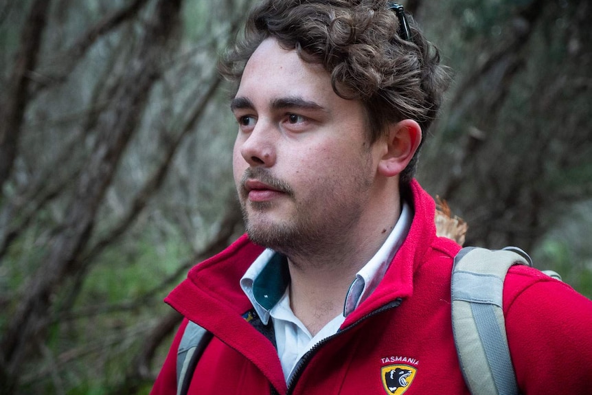 a portrait of Jye Crosswell in red parks and wildlife jacket under a ti-tree canopy on the walk into King's Run