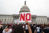 A woman standing in a large crowd holds a sign that says "No." in front of the US Capitol building